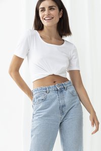 Biała krótka koszulka z okrągłym dekoltem i węzłem w talii; w połączeniu z jasnoniebieskimi, wysokimi dżinsami, lekko zniszczonymi.