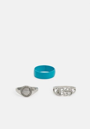 Três anéis: um de prata com um centro redondo e pequenas pedras, um de prata com letras texturizadas, e um anel sólido de turquesa.