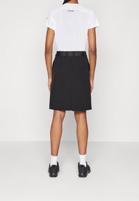 Pantalones cortos negros con una cinturilla texturizada, combinados con una camisa blanca de manga corta. El conjunto presenta un diseño minimalista y es adecuado para el uso casual.