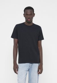 Juoda medvilninė trumpomis rankovėmis ir užapvalinta apykakle. Šiek tiek aptemptas dizainas, be matomų raštų ar grafikos. Dėvima su šviesiai mėlynomis džinsais.