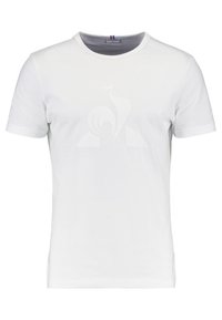 Valkoinen lyhythihainen t-paita pyöreällä kaula-aukolla, jossa on hillitty nostokirjailu rinnassa ja pieni raidoitettu etiketti kauluksessa.