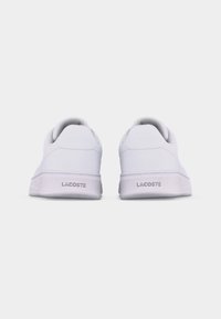 Par hvite Lacoste-sneakers vist bakfra, med merkets navn fremhevet på hælen av hver sko.