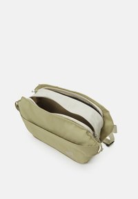 Bolsa de mensajero de tela verde con dos compartimentos, que presenta un exterior suave, cierre superior con cremallera y sutil detalle de logo.