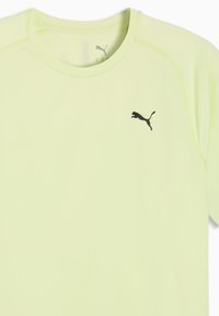 Ανοιχτό κίτρινο αθλητικό πουκάμισο με κοντά μανίκια και μαύρο λογότυπο Puma στη δεξιά πλευρά του στήθους.