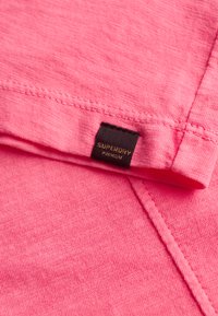 Lichtroze katoenen T-shirt met een gestructureerde afwerking. Voorzien van een zwart label met "Superdry Premium" op de kraag met gestikte details.