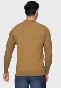Bruin gebreide trui met lange mouwen, een ronde halslijn en geribbelde zoom. Textuurdetails op de mouwen zorgen voor visuele aantrekkingskracht.
