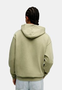 Sudadera de algodón verde oliva con capucha ajustable, corte relajado y puños de canalé. Tejido texturizado con un aspecto suave.