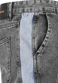 Vaqueros de denim negro con un panel insertado de color azul claro, acentuados con costuras de contraste y un bolsillo trasero visible.