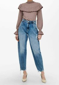 Pull côtelé marron clair avec encolure à volants, associé à un jean taille haute déchiré bleu clair et des escarpins crème.