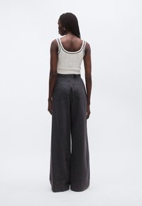 Tmavě šedé kalhoty s širokými nohavicemi a vysokým pasem, doplněné krémovým žebrovaným tílkem s černým lemováním a texturovaným vzorem.