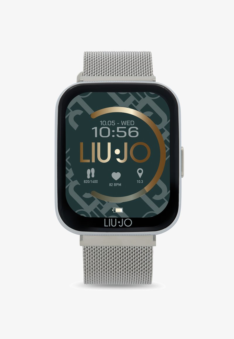 Orologio smartwatch con schermo quadrato, bracciale in rete metallica argentata. Il display mostra l'ora, la data e le metriche di fitness su uno sfondo scuro e con un motivo.