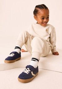 Baskets bleu marine en daim avec une bride en velcro, des lacets beige clair et une semelle en caoutchouc gomme. Détail de surpiqûres sur la tige.