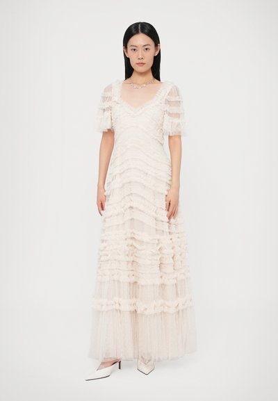 Μάξι φόρεμα από διαφανές ύφασμα, με στρώσεις βολάν σε ανοιχτό εκρού χρώμα. Λαιμόκοψη σε σχήμα V, μανίκια με φουσκάλες και υφή με τελείες. Απλά λευκά τακούνια.