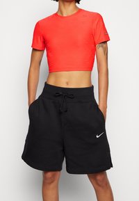 Röd kort sporttröja med präglade logotyper, tillsammans med svarta shorts med dragsko och en vit Nike swoosh-logotyp.