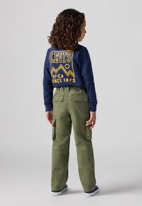 Maglietta a maniche lunghe blu navy con grafica gialla e testo, abbinata a pantaloni cargo verde oliva con più tasche e vestibilità rilassata.