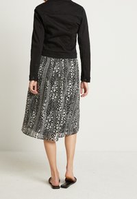 Svart denimjacka med långa ärmar i kombination med en flödande, knälång kjol med svart och vitt blommönster. Sandaler syns på fötterna.