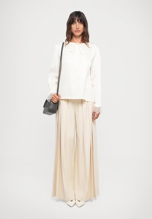 Hvit bluse med blonde mansjetter og snøring i halsen, sammen med vide beige bukser og en liten grå veske. Glatt stoff, enkelt design.