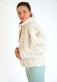 Pullover in pile color panna con una superficie texturizzata e morbida. Presenta un alto colletto, un cordino marrone e una patch del logo sulla manica.