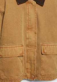 Barna vászon dzseki sötétbarnán szegélyezett gallérral, elülső zsebfedőkkel és a középső elülső részen varrott függőleges varrással.