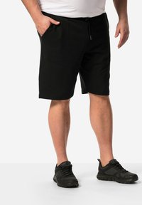 Černé sportovní kraťasy s elastickým páskem a šňůrkou, vybavené bočními kapsami. Nosené s černými sportovními botami.