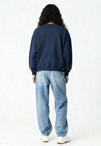 Marineblauwe oversized sweatshirt met verlaagde schouders, geribde manchetten, gecombineerd met lichtblauwe baggy jeans en witte sneakers. Achteraanzicht.