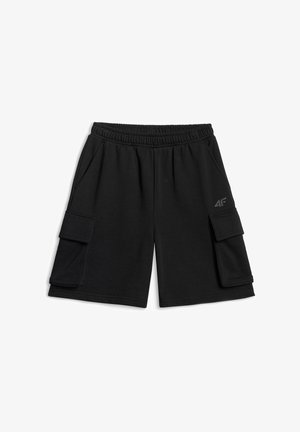 Garçon portant un short noir, un t-shirt noir, des chaussettes rayées et des baskets, tenant un ballon de volley-ball blanc et regardant légèrement vers le haut sur le côté.