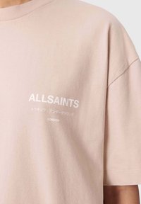 Lichtroze T-shirt gemaakt van zacht katoen, met een ronde hals en korte mouwen. Witte bedrukt merknaam en tekst op de voorkant.