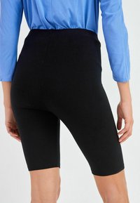 Shorts da ciclismo neri aderenti con una texture liscia, lunghi fino a metà coscia, design a vita alta, indossati con una maglietta blu a maniche lunghe.