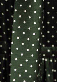 Zielony materiał w białe kropki, o gładkiej fakturze. Wzór jest równomiernie rozmieszczony, co daje spójny efekt wizualny.