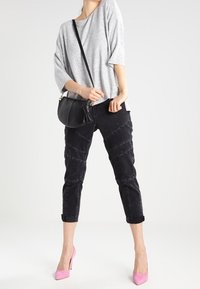 Šedý oversized pletený top, černé zúžené kalhoty s detailním švem a růžové vysoké podpatky. Černá krosbody taška s ramenním popruhem.
