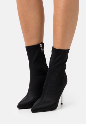 Stivaletti neri realizzati in tessuto elastico con punta affusolata, dotati di chiusura con zip e tacco a stiletto metallico.