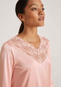 Lichtroze blouse met een V-hals ontwerp, voorzien van ingewikkelde bloemenkant langs de halslijn, gemaakt van zachte, gladde stof met lange mouwen.