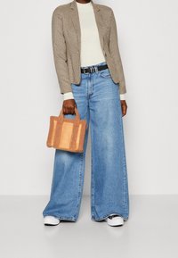 Brązowa kraciasta marynarka, kremowy top, szerokie niebieskie jeansy, czarny pasek, białe trampki oraz mała beżowo-brązowa futerkowa torebka.