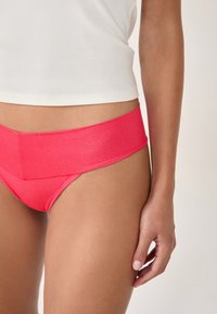 Rosa hochgeschnittene Unterwäsche mit glatter Textur und glänzendem Finish, ausgestattet mit einem breiten Bund und konturiertem Design für zusätzlichen Komfort.