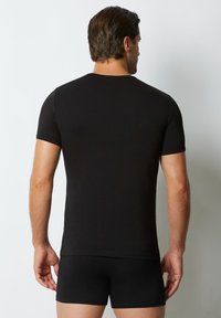 Tricou negru cu mânecă scurtă, confecționat dintr-un material moale, cu guler rotund și un design ajustat, purtat cu pantaloni scurți negri asortati.