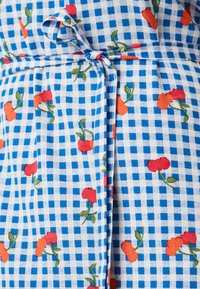 Μπλε και λευκό καρό ύφασμα με μικρά κόκκινα και πορτοκαλί λουλούδια. Περιέχει λεπτομέρεια ζώνης στη μέση και έχει λεία υφή.