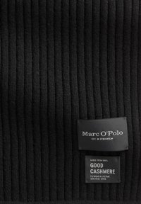 Tessuto di cashmere nero a coste con due etichette: "Marc O'Polo EST. IN STOCKHOLM" e "REALIZZATO CON 100% CASHMERE DI QUALITÀ". Superficie strutturata.