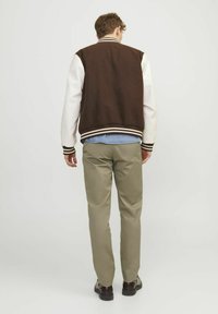 Veste varsity marron et crème avec un corps en laine, des manches en cuir, des poignets rayés, et une chemise en denim visible en dessous, portée avec un pantalon kaki.