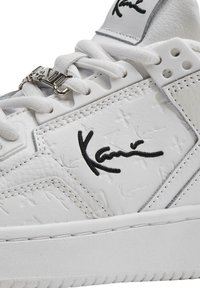 Baskets en cuir blanc avec dessus texturé, broderie de logo noir, verrou en métal pour les lacets et semelle en caoutchouc blanc avec un détail de couture.