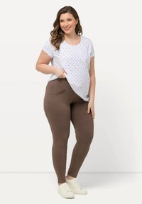 Camicetta bianca a maniche corte con pois neri, abbinata a leggings marroni con tasche laterali. Le sneakers bianche completano l'outfit.