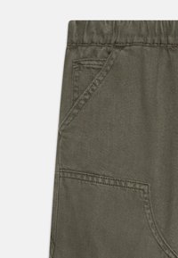 Pantalones de algodón en un verde oliva apagado, con una cinturilla elástica, bolsillo lateral y una tela texturizada sutil con detalles de costura.