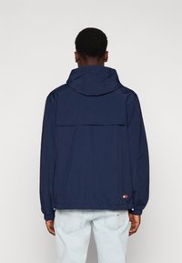 Tmavě modrá kapucí vybavená bunda z lehké tkaniny s elastickými manžetami a detailem zadní kapsy. Má minimalistický design bez ozdob.