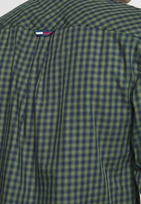 Camisa a cuadros verde y azul marino con tejido transpirable, cuello puntiagudo y un sutil detalle de pliegue en la espalda.