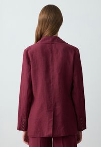 Bordowy blezer z lnu, z klapami, długimi rękawami i pojedynczym rozcięciem; posiada sześć guziczków na mankietach.