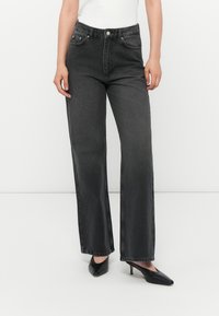 Høyt liv, vide denimjeans i mørkegrått med frontlommer og glidelås foran. Pare med svarte spisse hæler.
