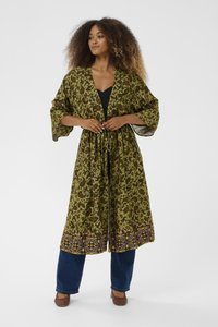 Zaļš rakstains kimono ar plašām piedurknēm, saplacinātu vidukli un dekoratīvu maliņu. Saskaņots ar tumšām džinsa biksēm un austām kurpēm.