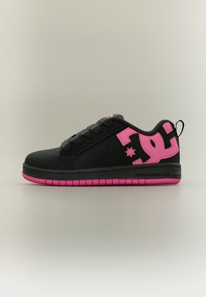 Μαύρο χαμηλό sneaker με ροζ σόλα, ροζ λογότυπο DC στη φτέρνα, μαύρα κορδόνια και θηλιά στο πίσω μέρος σε ουδέτερο φόντο.