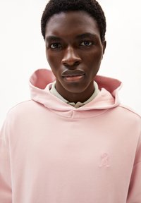 Felpa rosa chiaro con cappuccio accogliente, texture morbida e un piccolo logo ricamato in alto a sinistra. Il design presenta una vestibilità comoda.
