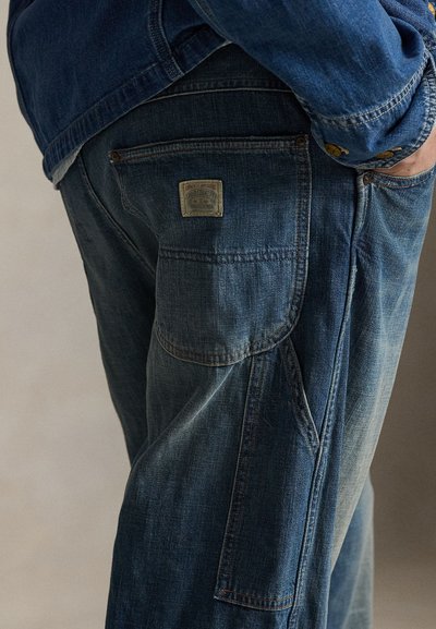 Μπλε τζιν παντελόνι με κλασικό σχέδιο, με εμφανές ετικέτα μάρκας στην πίσω τσέπη και αντίθετη ραφή.