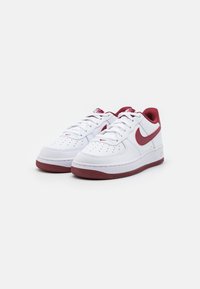 White Nike Air Force 1 sneakers with red accents. Features a smooth leather upper, round toe, and textured rubber outsole.